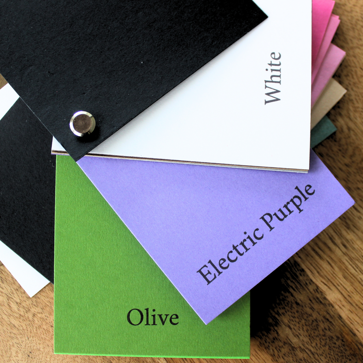 cardstock swatch book Color swatches labeled with names like White, Electric Purple, and Olive on a wooden surface.