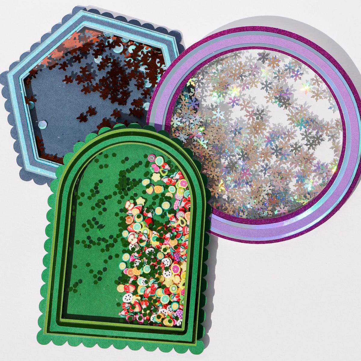 Three shaker cards made with clear acetate sheet windows, filled with snowflake sequins, fruit confetti, and gingerbread sequins in layered cardstock frames