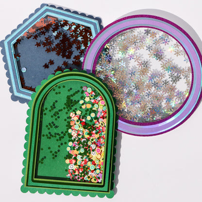 Three shaker cards made with clear acetate sheet windows, filled with snowflake sequins, fruit confetti, and gingerbread sequins in layered cardstock frames