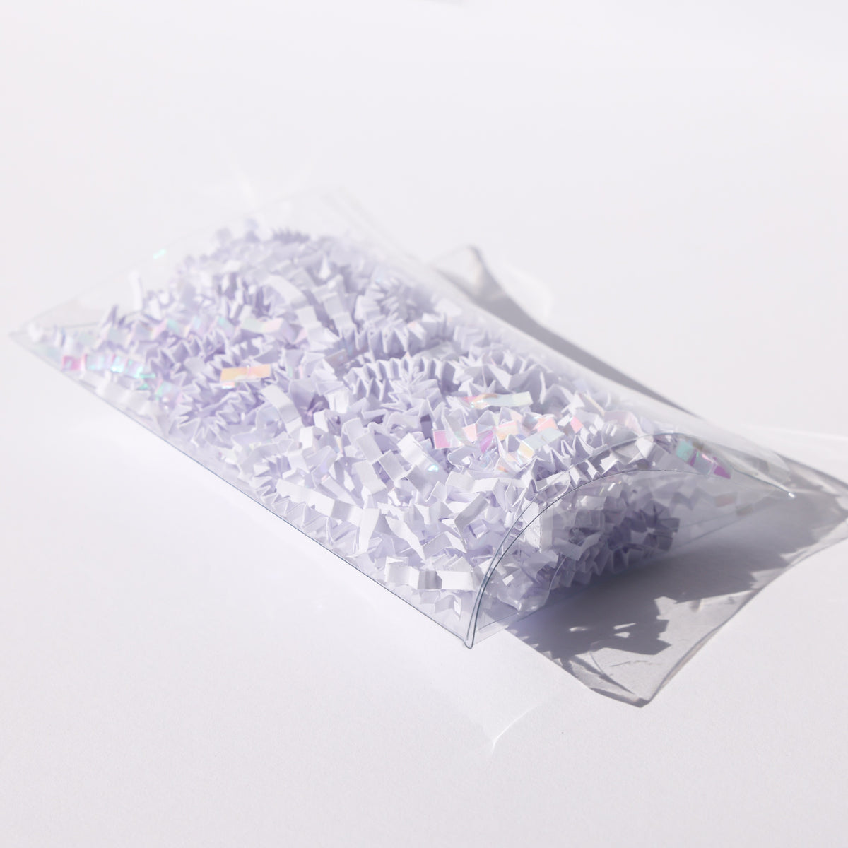 Clear acetate pillow box filled with white and iridescent paper shred, a party favor made from acetate sheets