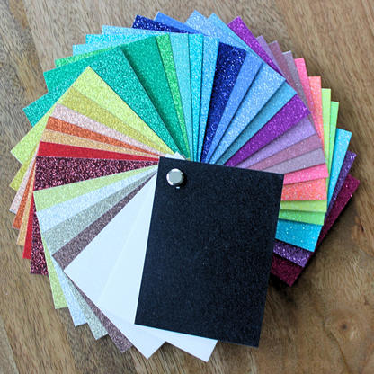 Glitter Cardstock Swatch Book collection of colorful glittery paper samples on a wooden surface. 