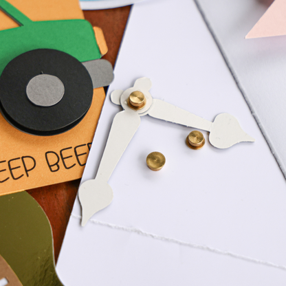 Gold cardstock spinner holding white cardstock clock hands on a card so the hands turn, with loose gold spinners beside it