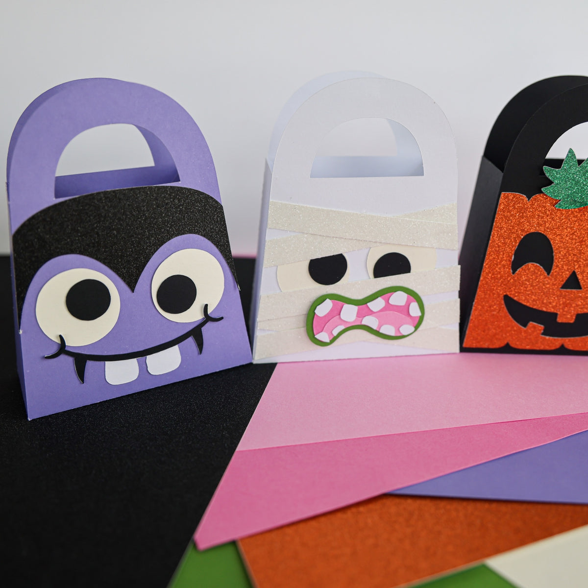 Vampire, mummy, and glitter pumpkin boo bags lined up on Halloween cardstock