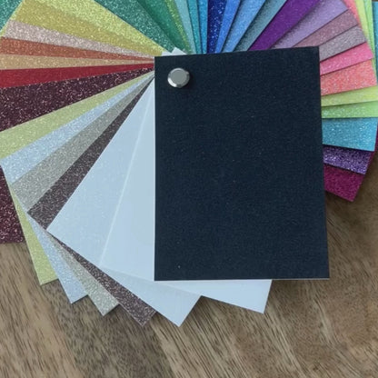 Glitter Cardstock Swatch Book collection of colorful glittery paper samples on a wooden surface. 