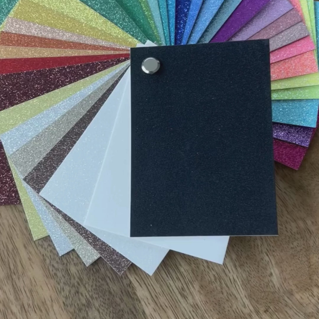 Glitter Cardstock Swatch Book collection of colorful glittery paper samples on a wooden surface. 