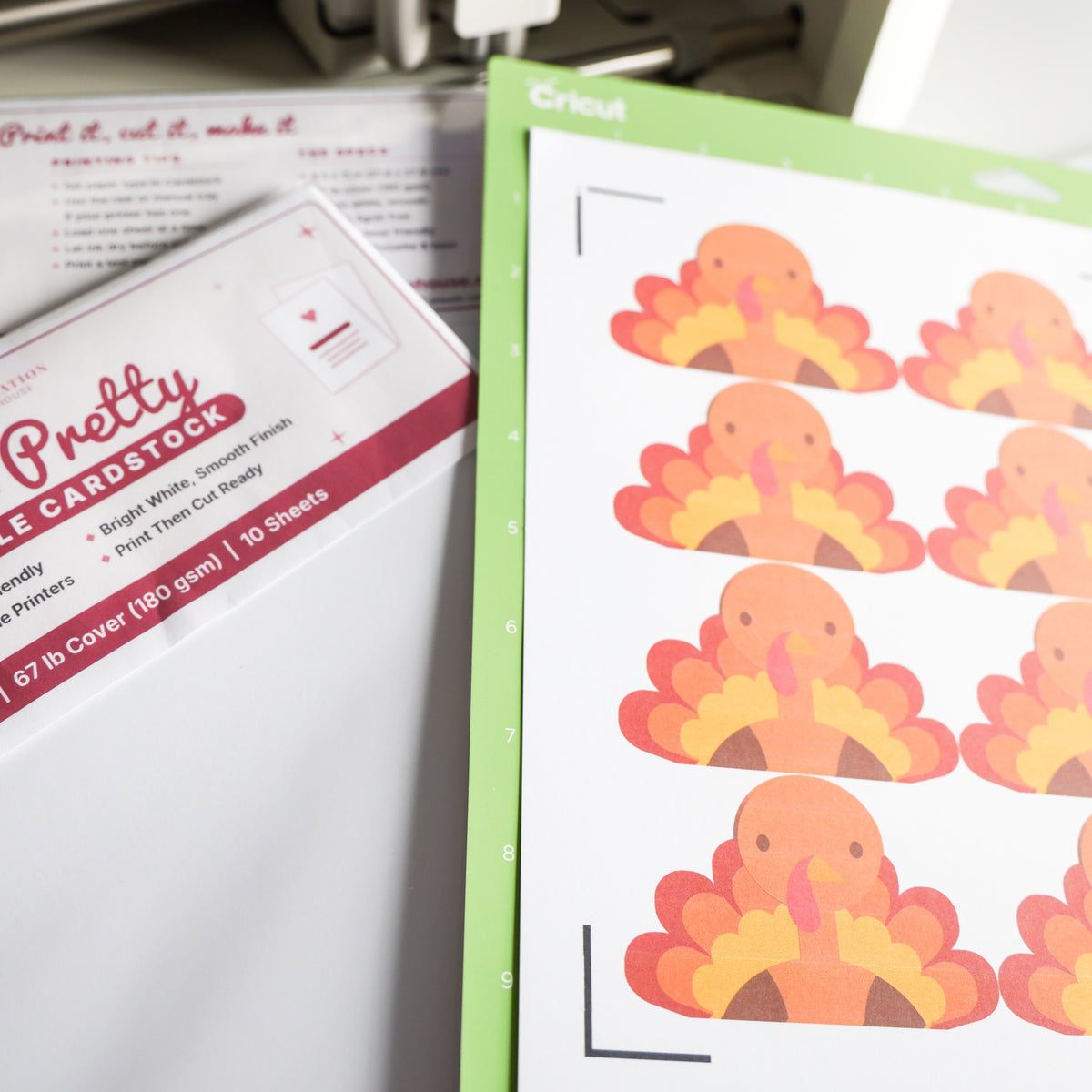 Printed white cardstock on a Cricut mat ready for Print Then Cut, next to the printable cardstock pack