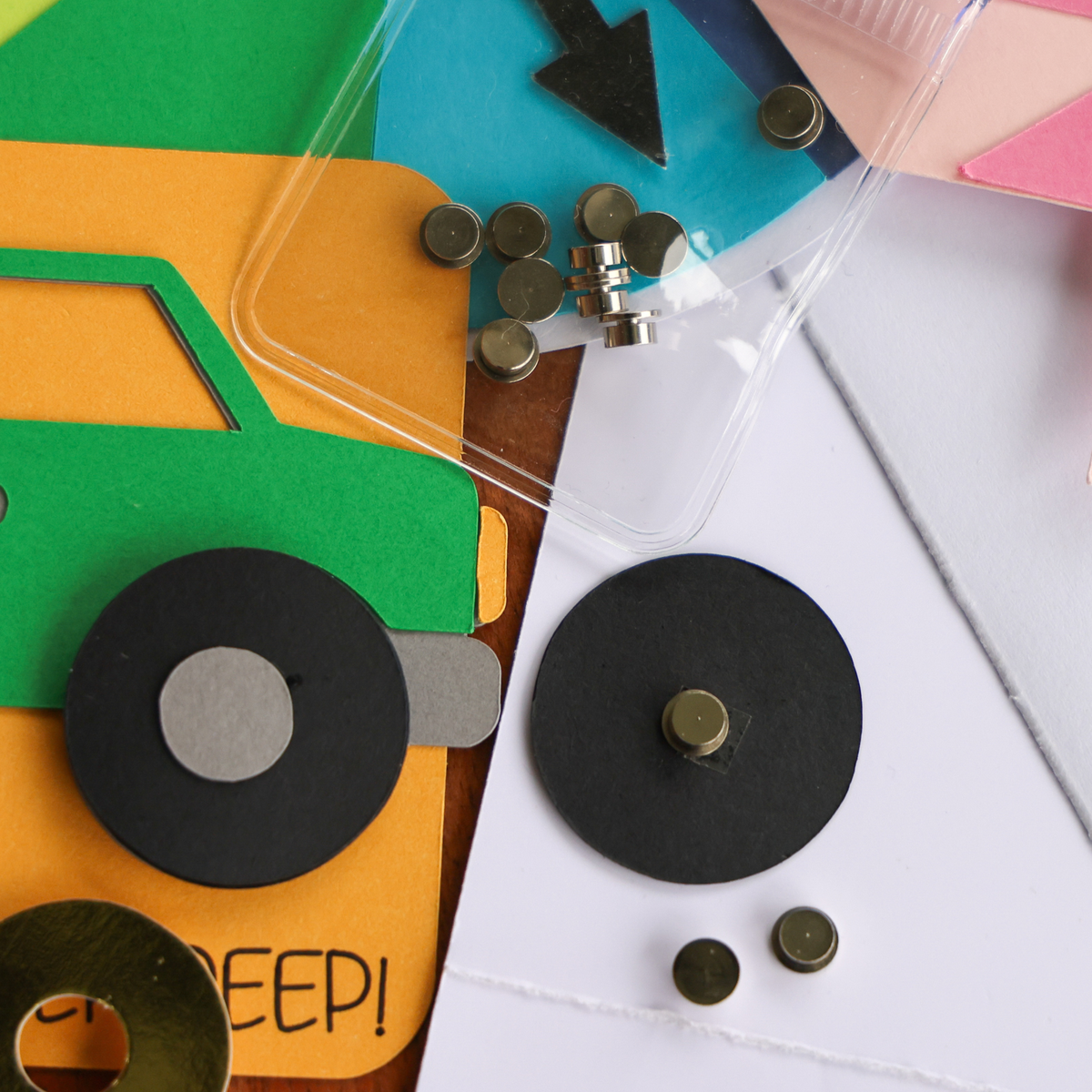 Silver cardstock spinner attached to the center of a black cardstock wheel on a white card, next to a truck card with spinning wheels