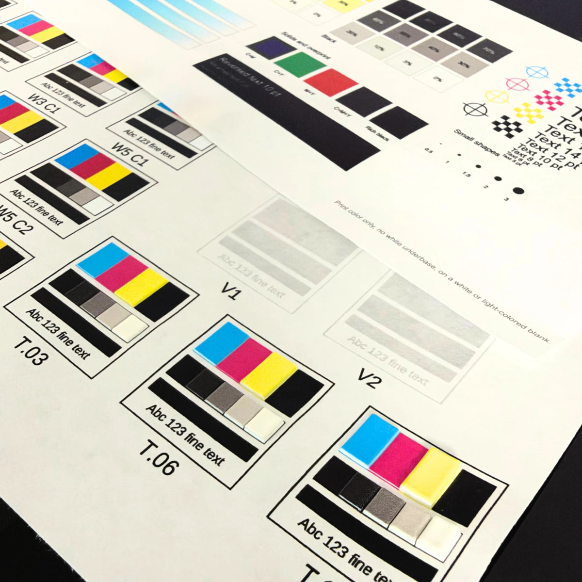 Raised UV printed texture swatches T.03, T.06, and T.10 next to glossy varnish swatches V1 and V2 on the UV printer test grid