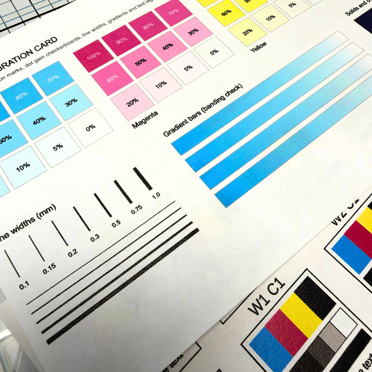 Close-up of the UV printed calibration card showing cyan and magenta ink density ramps, gradient bars for banding, and line widths from 0.1 to 1.0 mm